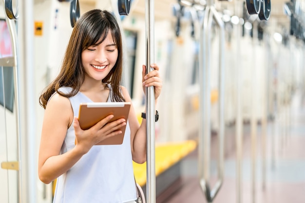 Young Asian woman passenger using social network via technology tablet in subway train