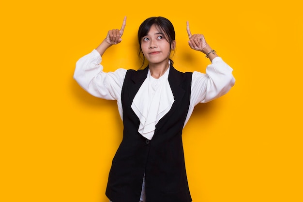 young asian woman pointing with fingers to different directions isolated on yellow background