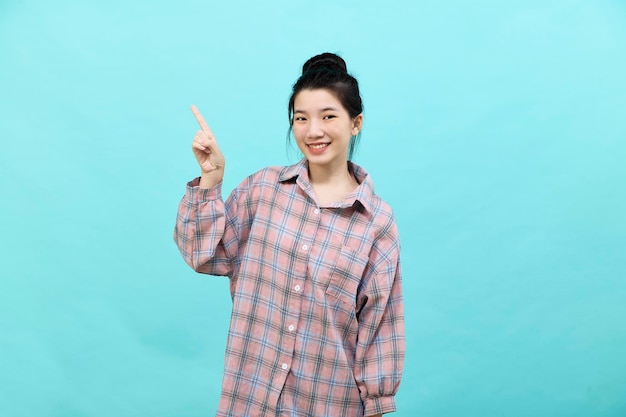 A young Asian woman pretty pointing looking at ads wearing a plaid shirt standing and feeling happy and confident on blue background