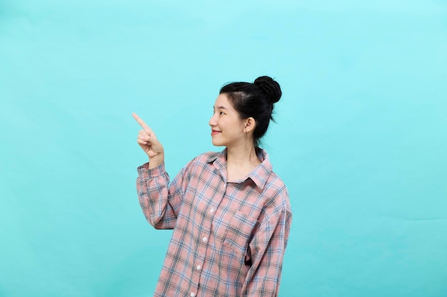 A young Asian woman pretty pointing looking at ads wearing a plaid shirt standing and feeling happy and confident on blue background