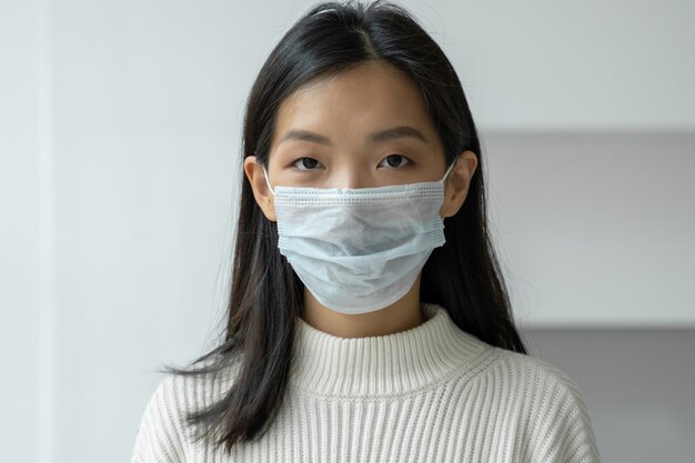 Young asian woman in a protective medical mask to protect against viral diseases looks into the