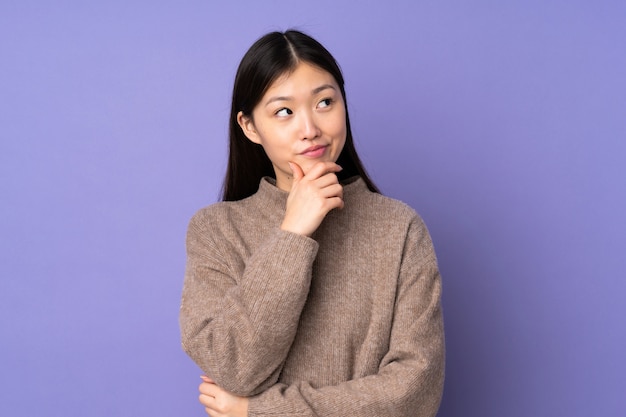 Young asian woman on purple wall thinking an idea while looking up