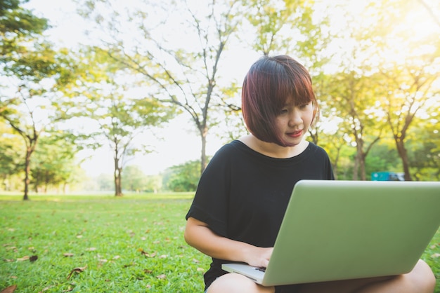 Young asian woman's legs on the green grass with open laptop