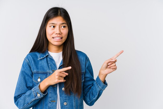 Young asian woman shocked pointing with index fingers to a blank space.