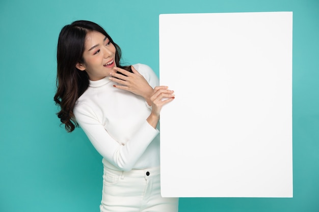 Young asian woman showing and holding blank white billboard isolated on green background