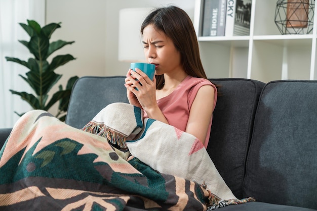 Young Asian woman sick on the sofa with temperature drinks hot