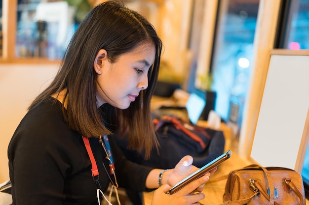 Young asian woman sitting and using smart phone at wooden counter in cafe at night