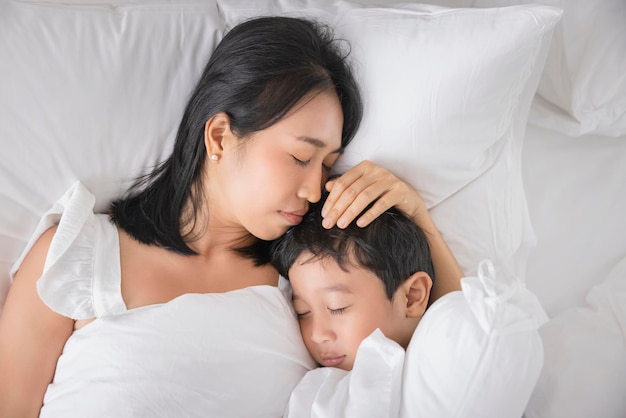 Young Asian woman and son sleeping in her bed and relaxing in bedroom they are lying on the side and relax with their eyes closed