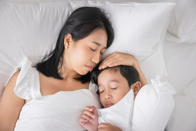 Young Asian woman and son sleeping in her bed and relaxing in bedroom they are lying on the side and relax with their eyes closed