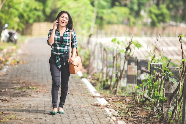 Young asian woman speaking on the phone while walking on the par