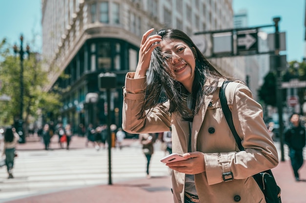 young asian woman standing in the street of morden city and looking happily and holding cell phone.