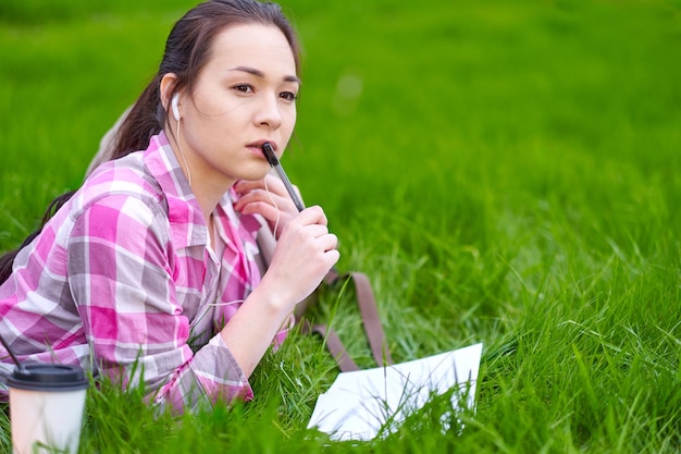 Young Asian woman Student with a book notebook and pen on grass meadow Preparation from session and exams outdoor portrait