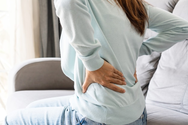 Young Asian woman suffering from backache sitting on couch in living room at home. Health problem concept. close up