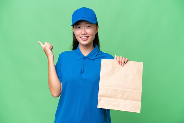 Young Asian woman taking a bag of takeaway food over isolated background pointing finger to the side