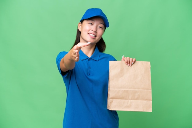 Young Asian woman taking a bag of takeaway food over isolated background shaking hands for closing a good deal