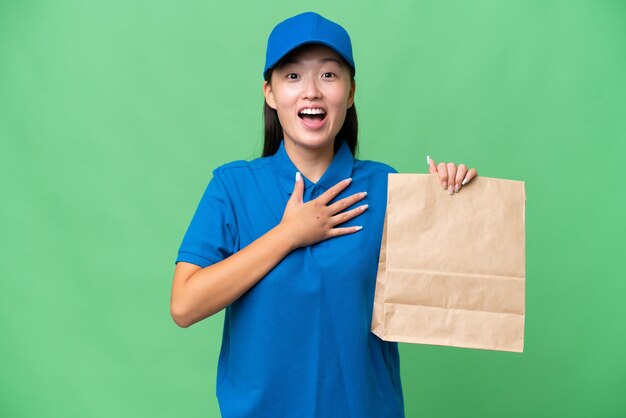 Young Asian woman taking a bag of takeaway food over isolated background surprised and shocked while looking right