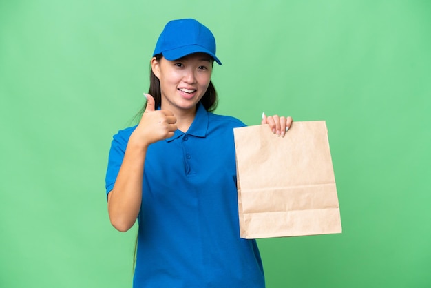 Young Asian woman taking a bag of takeaway food over isolated background with thumbs up because something good has happened