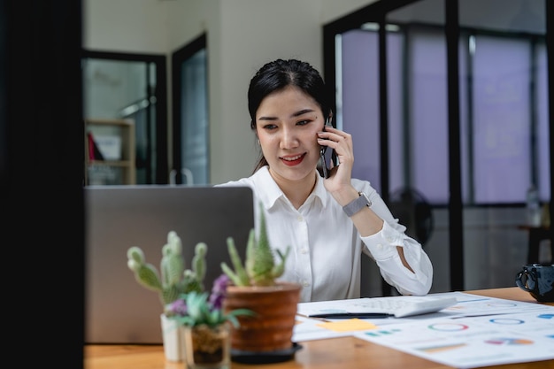 Young asian woman talking on the mobile phone and smiling while sitting at her working place in office