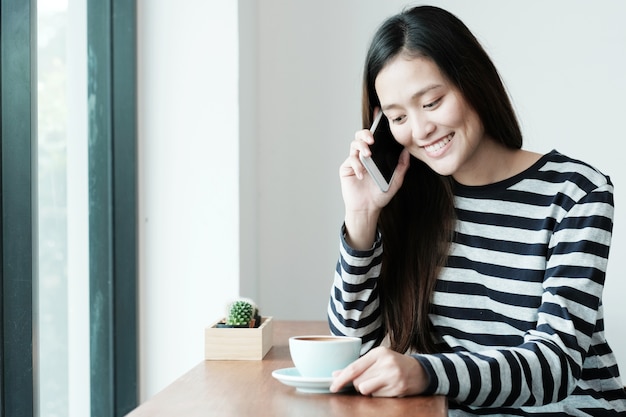 Young asian woman talking with smart phone while sitting by window cafe background