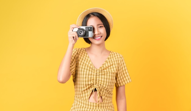 Young Asian woman tourist holding camera and looking on orange background