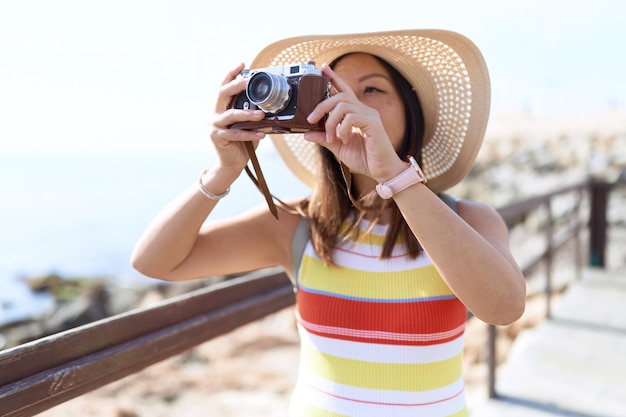 Young asian woman tourist using vintage camera at seaside