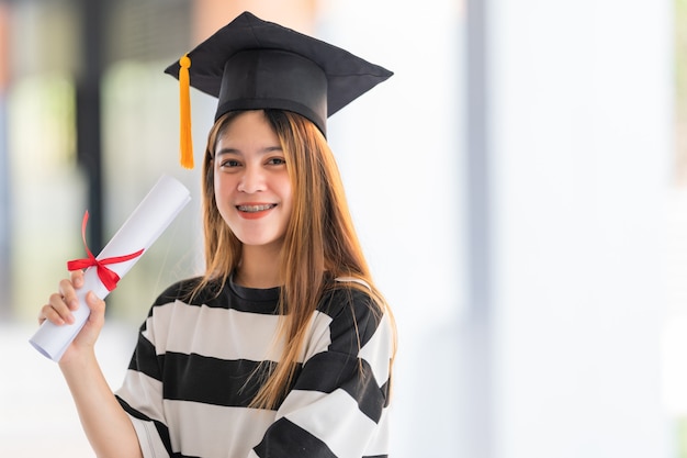 Young Asian woman university graduates in graduation gown and mortarboard hold a degree certificate