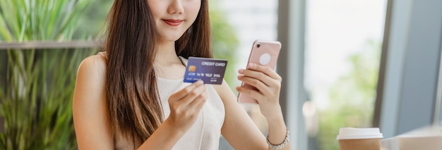 Young Asian woman using credit card with mobile phone for online shopping in coffee shop