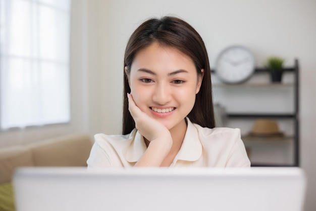 Young asian woman using laptop chatting video conference online sitting in living room at home Business Woman looking at screen Meeting on social media live steam Work learning from home