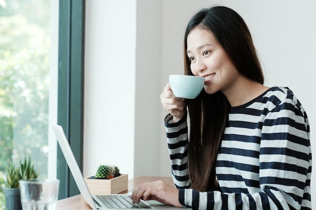 Young asian woman using laptop computer and drinking coffee at cafe background