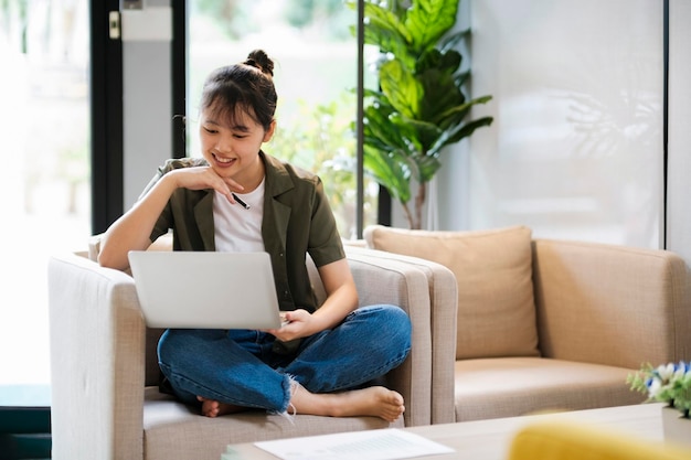 Young asian woman using laptop while leaning back on couch at homexA