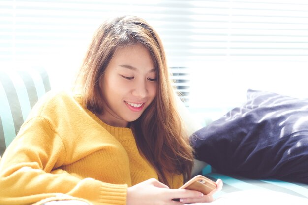 Young asian woman using smart phone sitting by window background