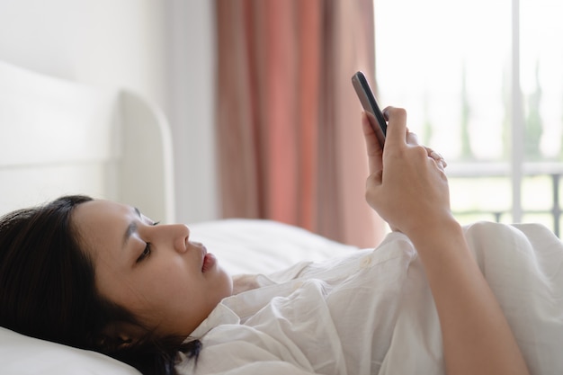 Young asian woman using smartphone with blank screen while lying in bed at morning.