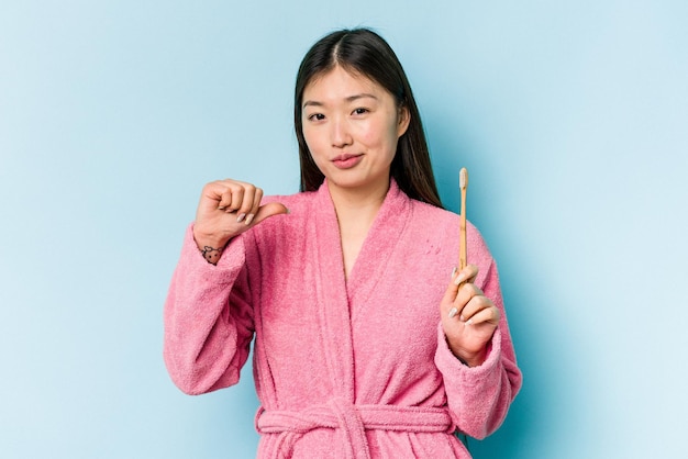 Young asian woman wearing a bathrobe brushing teeth isolated on pink background feels proud and self confident example to follow