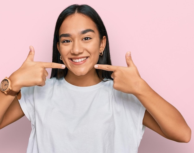 Young asian woman wearing casual white t shirt smiling cheerful showing and pointing with fingers teeth and mouth dental health concept