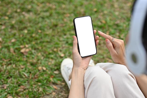 Young Asian woman wearing headphones and using phone relaxing on grass in the public park