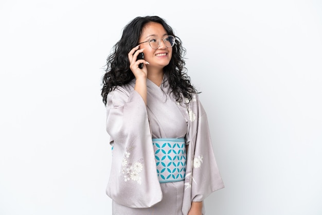 Young asian woman wearing kimono isolated on white background keeping a conversation with the mobile phone