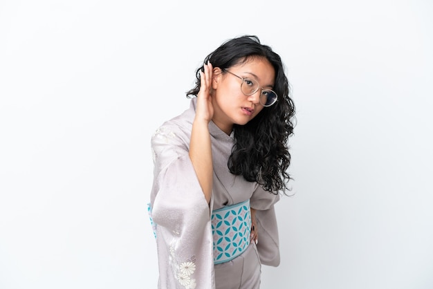 Young asian woman wearing kimono isolated on white background listening to something by putting hand on the ear