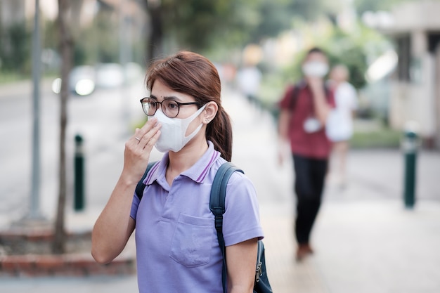 Young Asian woman wearing N95 respiratory mask protect and filter pm2.5 (particulate matter) against traffic and dust city. healthcare and air pollution concept