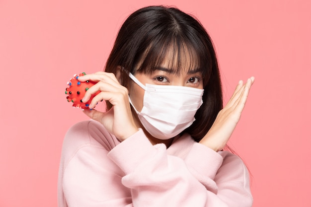 Young asian woman wearing protection mask or surgical mask for protected virus and air pollution making cross hand stop and hold virus on hand on pink wall,Health care and coronavirus concept