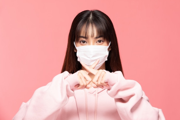 Young asian woman wearing protection mask or surgical mask for protected virus and air pollution making cross hand stop virus on pink wall,Health care and coronavirus concept