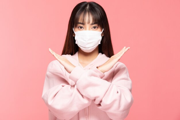 Young asian woman wearing protection mask or surgical mask for protected virus and air pollution making cross hand stop virus on pink wall,Health care and coronavirus concept