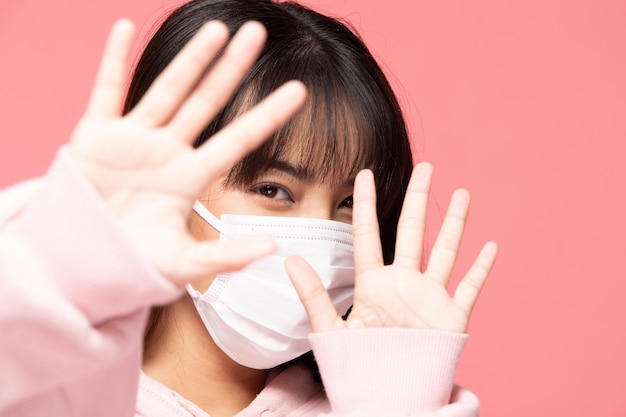 Young asian woman wearing protection mask or surgical mask for protected virus and air pollution making hand stop virus on pink wall,Health care and coronavirus concept