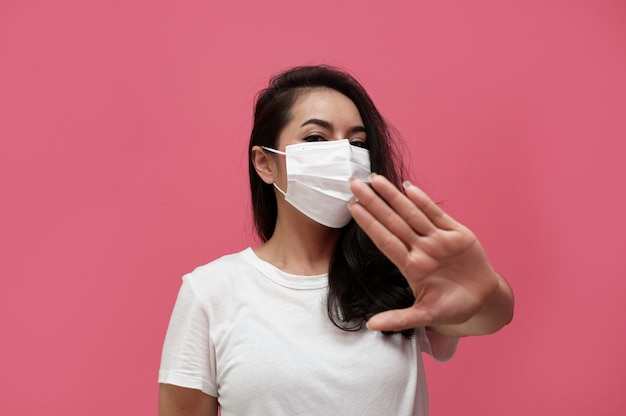 young asian woman wearing protection mask or surgical mask for protected virus and air pollution making hand stop virus on pink wall ,Health care and coronavirus concept