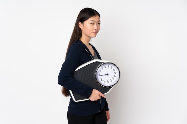 Young asian woman on white wall with weighing machine