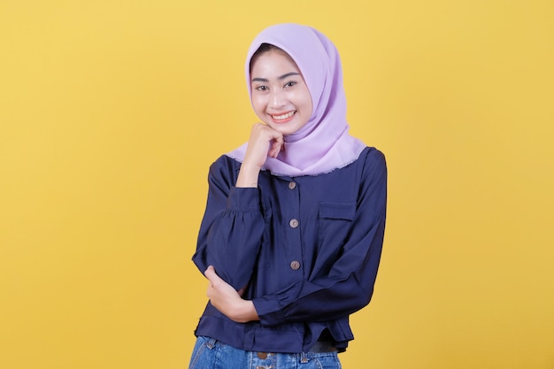 Young Asian woman who is positive with a cheerful smile on the face wearing a hijab and casual clothes in the room is yellow.