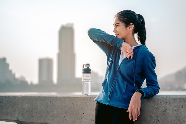 Young asian woman wipes sweat after a morning workout in the city A city that lives healthy in the capital Rear view of the city Exercise fitness jogging running lifestyle healthy concept