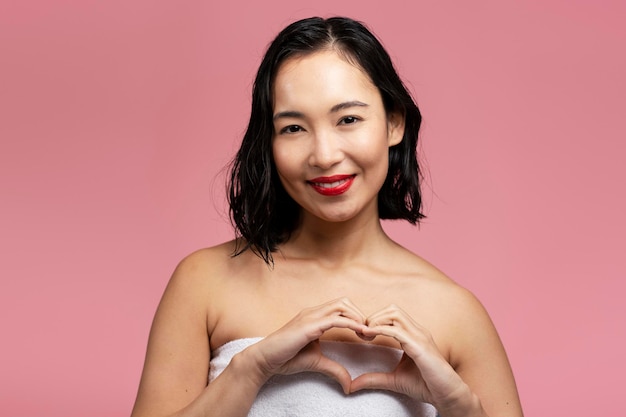 Young asian woman with bare shoulders showing heart shape with hands