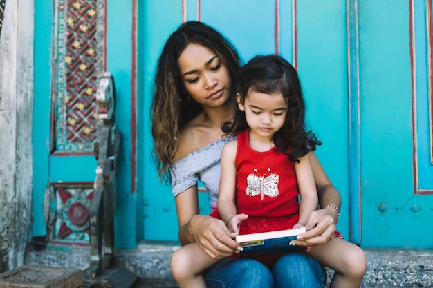 Young Asian woman with book and preschool daughter on knees