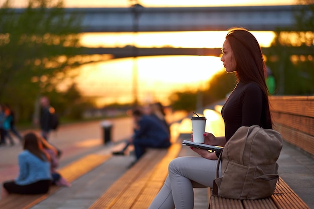 Young asian woman with coffee and book in the evening at sunset outdoor city portrait