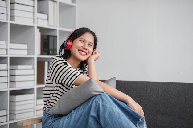 Young asian woman with headphones relaxing at home listening to music sitting on cozy sofa wearing headphone